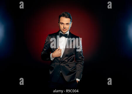Professionelle Schausteller tragen Anzug steht auf schwarzen und roten Hintergrund posiert für die Kamera lächelnd verspielt Stockfoto