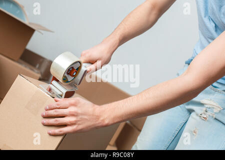 Jungen blonden Mann, der seinen neuen Platz, der Holding Scotch Tape packen Dinge konzentriert Stockfoto