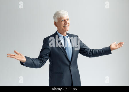 Senior Business mann Studio stehen auf graue Wand Hände isoliert beiseite, Raum suchen Kamera lächeln positive Seite anzeigen Stockfoto