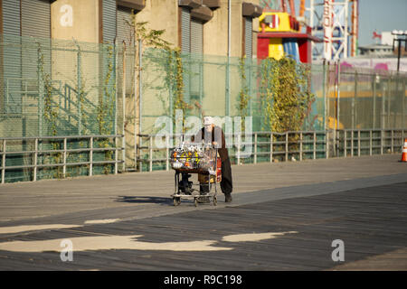 Ein obdachloser Mann drückt eine Warenkorb voller Zeug auf Coney Island Beach gesammelt. Stockfoto