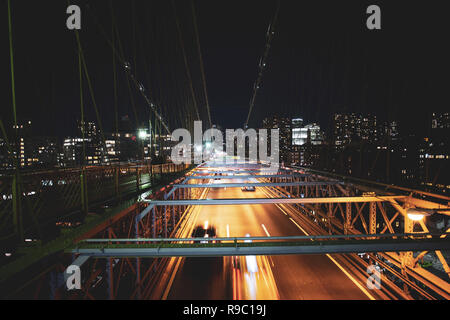 Lange Belichtung Bild von Autos vorbei über die beleuchteten Brooklyn Bridge bei Nacht. Im Hintergrund die Skyline von Manhattan, New York City, USA. Stockfoto