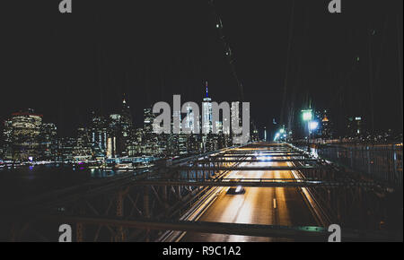 Lange Belichtung Bild von Autos vorbei über die beleuchteten Brooklyn Bridge bei Nacht. Im Hintergrund die Skyline von Manhattan, New York City, USA. Stockfoto