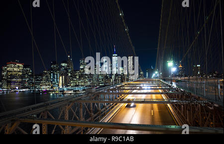 Lange Belichtung Bild von Autos vorbei über die beleuchteten Brooklyn Bridge bei Nacht. Im Hintergrund die Skyline von Manhattan, New York City, USA. Stockfoto