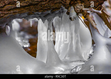 Gefrorenen Eiszapfen hängen von log in Stream Stockfoto