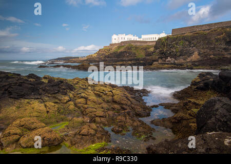 Cliff Walk in Port Stewart, Nordirland mit dem Dominican College sichtbar auf der Klippe und Flechten und Seegras bedeckte Felsen im Vordergrund. Stockfoto