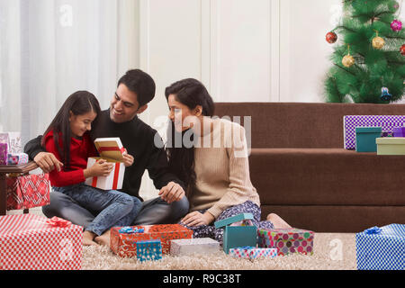 Mädchen öffnen der Weihnachtsgeschenk mit Eltern zu Hause Stockfoto