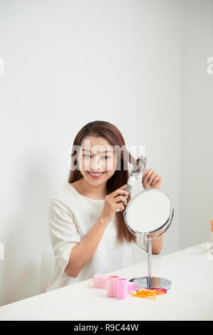 Das Loswerden von Kabelsalat. Schöne junge Frau an ihr Spiegelbild in mirrorand ihr langes Haar bürsten Während am Tisch sitzen Stockfoto