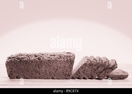 Lange Roggenbrot in Scheiben geschnitten auf hölzernen Tisch von der Seite. Selektiver Fokus auf das Brot. Sepia getont Schwarz/Weiß-Bild Stockfoto
