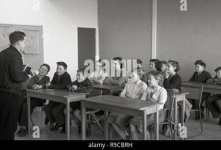 1955, historische, Gruppe der Grundschüler in einem Klassenzimmer, am Schreibtisch sitzend, von einem jungen erwachsenen männlichen Lehrer, der sich direkt im Gespräch mit den Kindern, vor Ihnen und nicht an einer Tafel, England, UK gelehrt wird Stockfoto