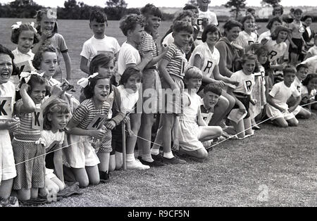 1950, historische, Schulkinder sitzen auf einer Rasenfläche jubelnd auf mitkonkurrenten an einer Grundschule Sport Tag, England, UK. Stockfoto