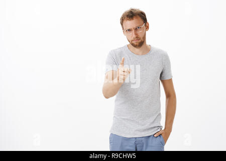 Fokussierte männliche Unternehmer mit Wegbeschreibungen auf Aufgabe streng und ernst mit Mitarbeitern zitternden Zeigefinger, bei camera Pointing, unzufrieden oder mit schlechten Arbeit enttäuscht über weiße Wand Stockfoto