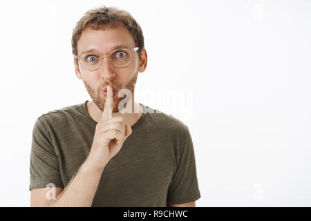 Um es Überraschung halten. Portrait von Lustig lustig und fröhlich attraktiven männlichen Erwachsenen mit Borsten falten Lippen in shhh Sound holding Zeigefinger über Mund, während shushing Geheimnis zu speichern. Stockfoto