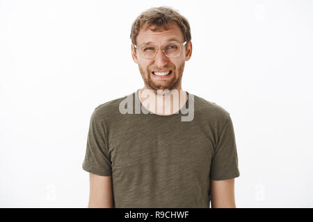 Guy schielen und lustiges Gesicht Essen saure Zitrone runzelte die Stirn und Faltenbildung Nase ständigen empört und auf weißem Hintergrund in transparenten Gläser und grünem T-Shirt unzufrieden Stockfoto