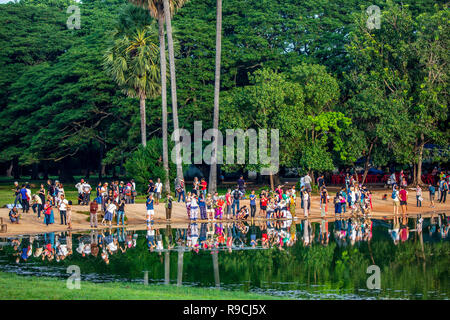 Touristen beobachten Sonnenaufgang über einem Teich mit grünen Bäumen im Hintergrund bei Tempelanlage Angkor Wat, Siem Reap, Kambodscha. Stockfoto