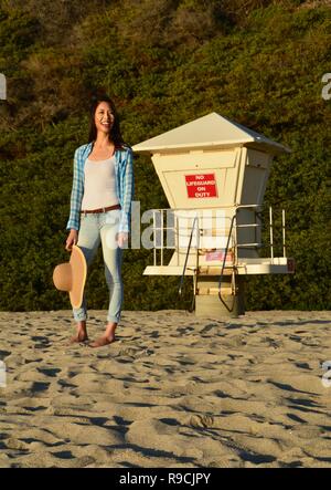 Lächelnd, Entspannt, schöne Frau stand vor einer unbemannten Rettungsschwimmer stehen am Strand. Laguna Beach, CA. Stockfoto