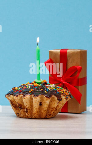 Lecker geburtstag Cupcake mit Schokoladenüberzug und Karamell, mit brennenden Kerzen und festlichen Geschenkverpackung auf blauem Hintergrund eingerichtet. Happy birthday minimal Stockfoto