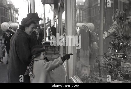 1950, historische, ein Kind mit Ihren Eltern in einer Straße in ein spielzeuggeschäft Fenster. Stockfoto