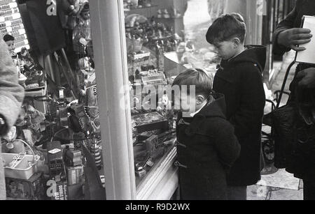 1950, historische, zwei Jungen tragen duffel Mäntel außerhalb in einer Straße in ein spielzeuggeschäft Fenster, England, Großbritannien Stockfoto