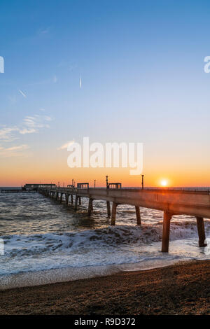 Sonnenaufgang in klaren, blauen und gelben Himmel über den Englischen Kanal und Pier an der Küste von Kent. Abgehackt, raue See stürzt am Kiesstrand. Stockfoto