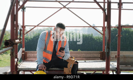 Mann bei der Arbeit In Baustelle lächelnd und mit Smartphone Stockfoto