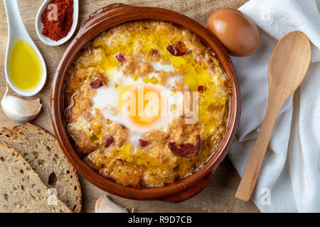 Knoblauch und Brotsuppe (Kastilisch, aus Spanien) in Lehmtöpfen und seine wichtigsten Bestandteile. Blick von oben. Holz Hintergrund Stockfoto