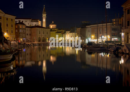 Piran, Slowenien. Die Nacht auf dem zentralen Platz der slowenischen Küstenstadt wie vom Hafen gesehen. Ansicht aller beleuchteten Gebäuden. Stockfoto