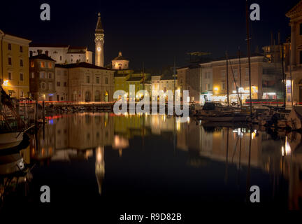 Piran, Slowenien. Die Nacht auf dem zentralen Platz der slowenischen Küstenstadt wie vom Hafen gesehen. Ansicht aller beleuchteten Gebäuden. Stockfoto