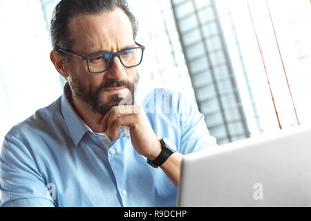Reifer mann Händler Tragen von Brillen am Tisch im Cafe am Tag sitzen an Laptop überwachung Stocks auf der Suche konzentrierte close-up Stockfoto