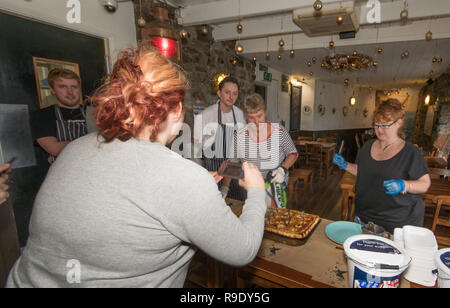 Fowey, Cornwall, UK. 23 Dez, 2018. Ein Besucher der Ship Inn eine Fotografie des traditionellen Stargazy pie in The Ship Inn bei Mousehole, mit der Wirtin, Restaurant Personal und Koch im Hintergrund. Der fisch Pie mit Sardine Köpfe und Schwänze, stößt, ist in der Kneipe auf Tom Bawcocks Eve Die Geschichte geht, dass Tom, ein aus dem 16. Jahrhundert Fischer, trotzte Stürmen und verfing sich genug Fisch im ganzen Dorf zu füttern. Foto: Simon Maycock/Alamy leben Nachrichten Stockfoto