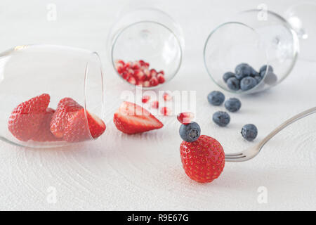 Heidelbeeren, Erdbeeren und Granatapfel Samen in Weingläser und Beeren auf eine Gabel, weißer Hintergrund Stockfoto