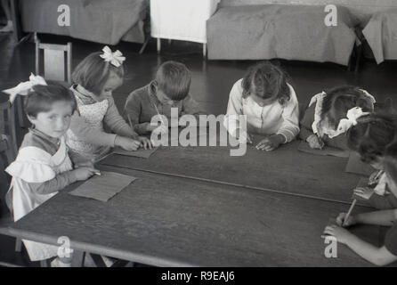 1948, nach dem Zweiten Weltkrieg Großbritannien, Bild zeigt eine Gruppe von osteuropäischen Flüchtlingskinder sitzen zusammen mit Papier und Bleistift an einem Holztisch in Ihrem Wohnraum. Ihre kleinen Camp Betten gesehen werden kann. Stockfoto