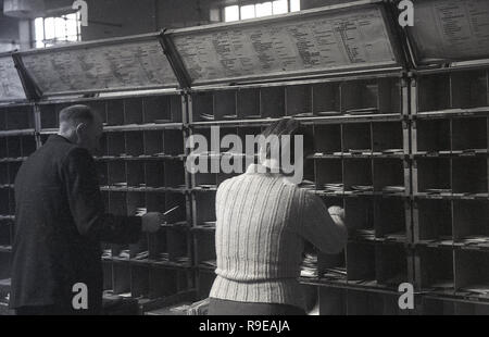 1948, historisch, zwei Mitarbeiter des General Post Office (GPO), die in einem Postsortierbüro in England, Großbritannien arbeiten. Das Bild zeigt, wie sie Briefe in kleine Kabinen für die verschiedenen Straßen legen. Stockfoto