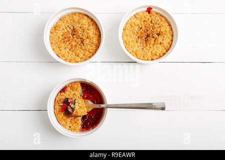 Drei bröckelt mit Himbeeren, Stachelbeeren, Brombeeren und Zimt. Englisch Dessert in einem weißen Keramik Form zum Backen auf weissem Holztisch. Zu Stockfoto