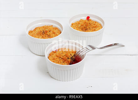 Drei bröckelt mit Himbeeren, Stachelbeeren, Brombeeren und Zimt. Englisch Dessert in einem weißen Keramik Form zum Backen auf weissem Holztisch Stockfoto