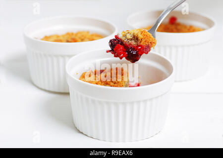 Stück mit Himbeeren, Stachelbeeren, Brombeeren und Zimt auf Gabel zerbröseln. Englisch Dessert in einem weißen Keramik Form zum Backen auf weißem Holz- Stockfoto