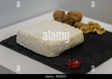 Tomino Käse auf Schwarz Tischdecke mit kleinen roten Beeren und Nüssen dekoriert. Stockfoto