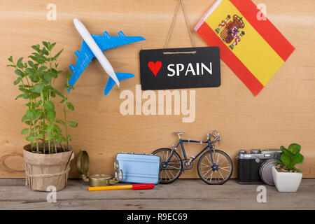 Reisezeit - Tafel mit dem Text 'Liebe', Spanien Flagge Spanien, Modellflugzeug, Kamera, Fahrrad auf braunem Holz- Hintergrund Stockfoto