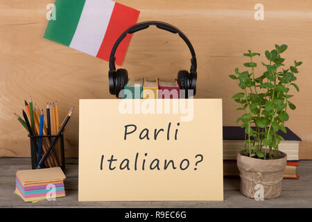 Sprachen lernen Konzept - Papier mit Text "parli Italiano?", Flagge der Italia, Bücher, Kopfhörer, Bleistifte auf hölzernen Hintergrund Stockfoto