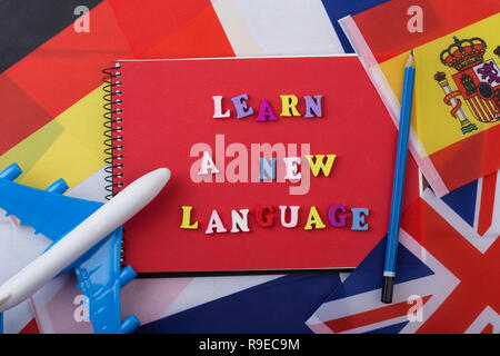Sprachen lernen Konzept - rot Notepad und bunte Buchstaben aus Holz mit Text' Lernen Sie eine neue Sprache', Fahnen, Modellflugzeug, Bleistift Stockfoto