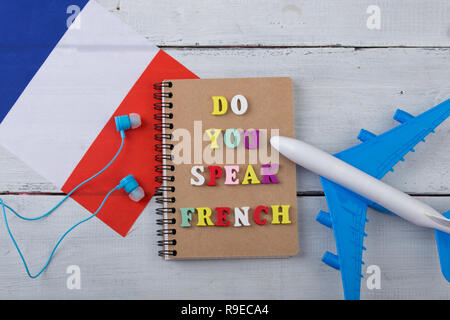 Konzept des Lernens der französischen Sprache - bunte Buchstaben mit dem Text 'Französisch', Flagge der Frankreich, Flugzeug sprechen, Kopfhörer auf weißem Holz- hinterg Stockfoto