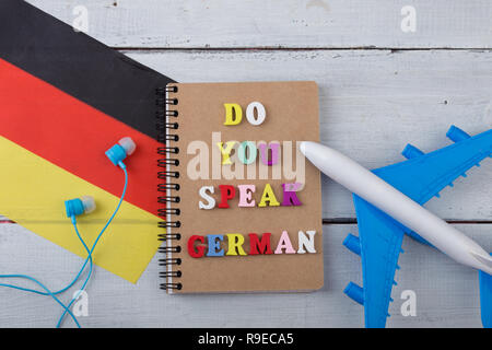 Konzept des Lernens der deutschen Sprache - bunte Buchstaben mit Text "o du Deutsch', Flagge der Deutschland, Flugzeug sprechen, Kopfhörer auf weißem Holz zurück Stockfoto