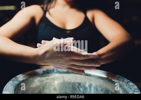 7/8 Schuß von jungen weiblichen Athleten Händeklatschen mit Kreide Pulver vor dem Krafttraining. Stockfoto