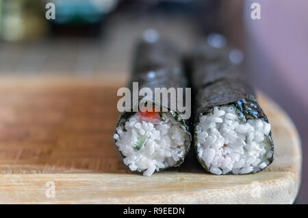 Die Sushi Rollen zu Hause: Zwei Shaped Round Brötchen Abdichtung auf einem Holzbrett vor dem Schneiden. Verschwommen Küche Tisch im Hintergrund Stockfoto