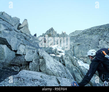 Bergführer suchen, um sich auf einem felsigen Aufstieg in den französischen Alpen mit Seil Teams vor ihm Stockfoto