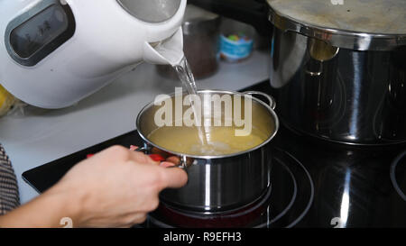 Kaukasische Frau gießen heißes Wasser in den Topf, kochen traditionelle Suppe, Nudeln, Nahaufnahme, niemand Stockfoto