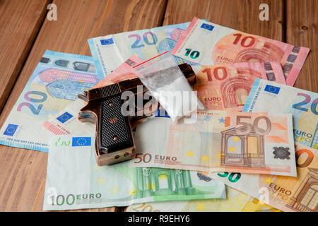 Schwarze Pistole und Pakete von Drogen vor dem Hintergrund der Euro auf einem Holztisch. Stockfoto