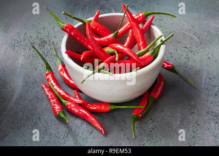 Nahaufnahme auf red hot chili peppers in Keramik Schüssel über dunkel strukturierten Tabelle. Essen Hintergrund. Stockfoto
