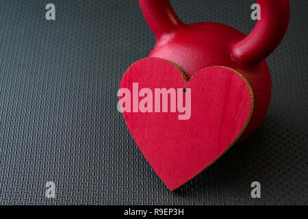 Red kettlebell auf einem schwarzen Turnhalle Boden mit großen roten Herz Valentinstag Fitness zu feiern. Stockfoto