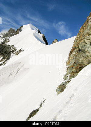 Bergsteiger auf einem steilen und schmalen Schneegrat führt zu einem hohen Gipfel in den Schweizer Alpen Stockfoto