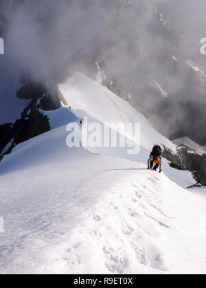 Bergsteiger auf einem steilen und schmalen Schneegrat führt zu einem hohen Gipfel in den Schweizer Alpen Stockfoto